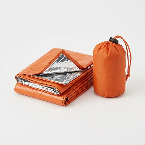 Orange emergency bivvy sack folded with the silver reflective inside showing, next to its small orange drawstring stuff sack