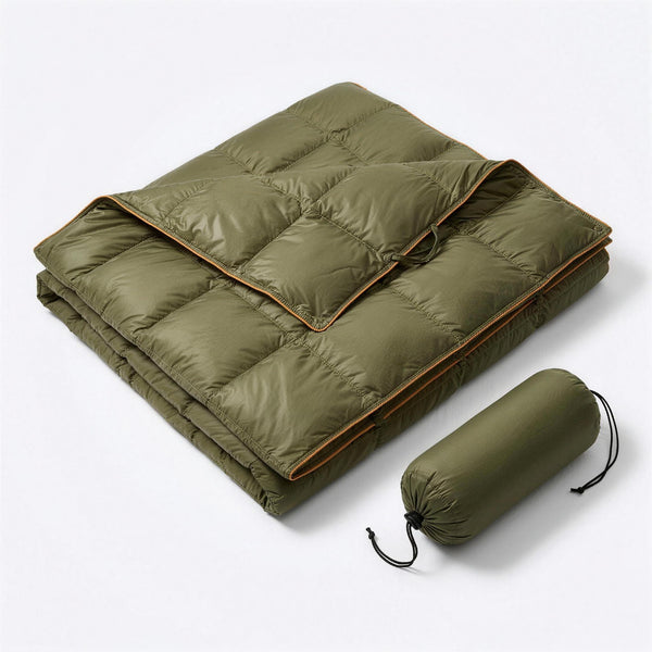 Green puffer blanket with orange piping, folded with one corner turned back, next to its green drawstring stuff sack