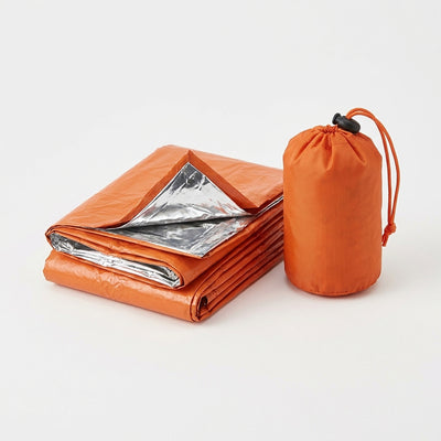 Orange emergency bivvy sack folded with the silver reflective inside showing, next to its small orange drawstring stuff sack