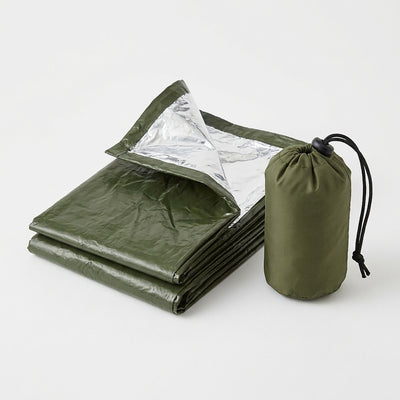 Green emergency bivvy sack folded with the silver reflective inside showing, next to its small green drawstring stuff sack
