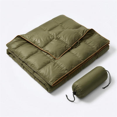 Green puffer blanket with orange piping, folded with one corner turned back, next to its green drawstring stuff sack