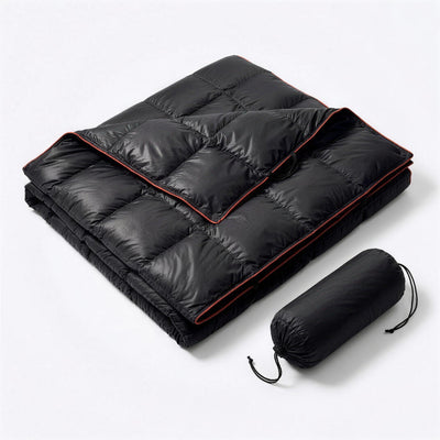 Black puffer blanket with red piping, folded next to its black drawstring stuff sack