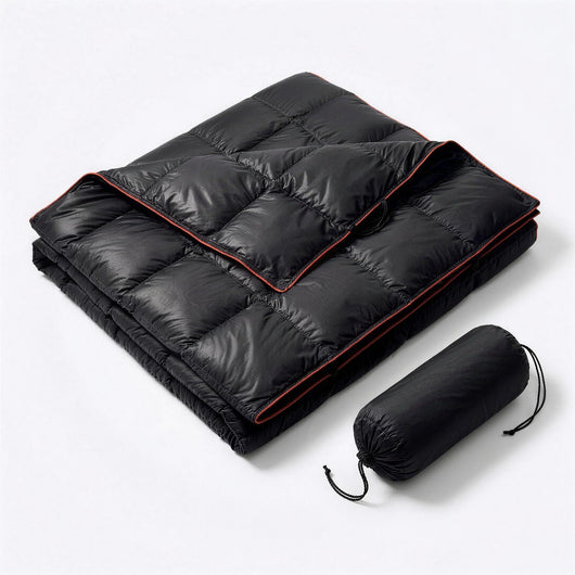 Black puffer blanket with red piping, folded next to its black drawstring stuff sack