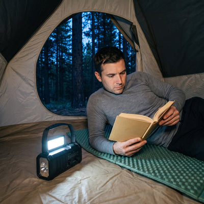 Man reading a book in a tent by the fold-up reading light of the emergency radio