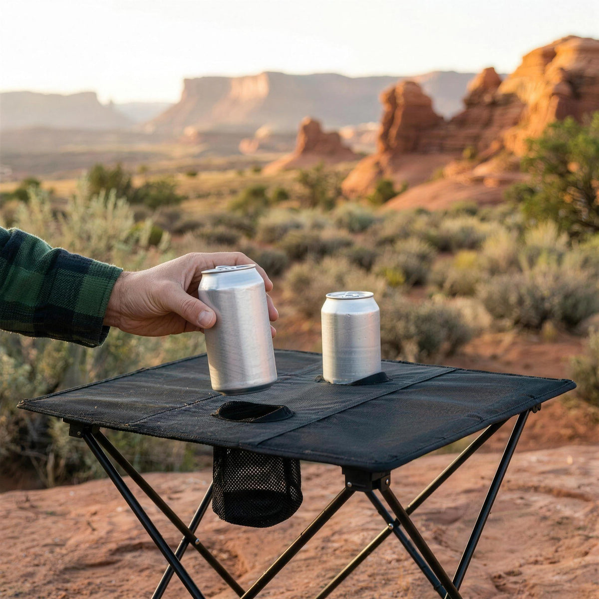 Hand lifting a can out of one of the two cup holders on the folding camping table