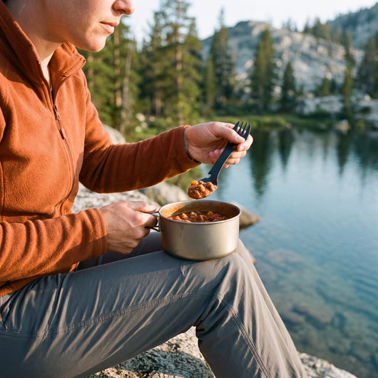Hiker eating chili from a camp pot with the black camping spork beside an alpine lake