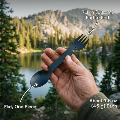 Black camping spork held in a hand by a mountain lake: 7.1 in (18 cm) end to end, about 1.6 oz (45 g) each, flat and in one piece