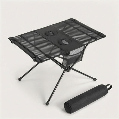Black folding camping table with two cup holders and a mesh side pocket, next to its black carry bag
